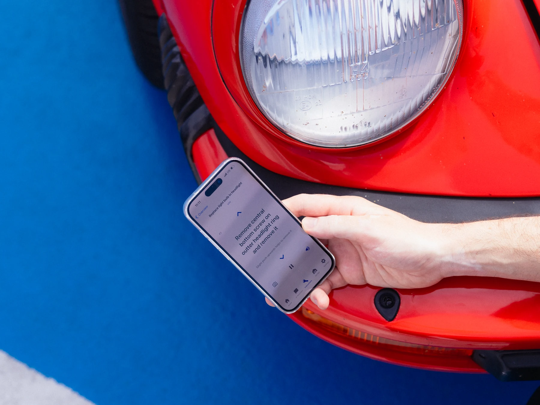 MINT Instructions App im Einsatz: Schritt-für-Schritt-Anleitung zum Ausbau eines Scheinwerfers auf dem Smartphone, direkt am Scheinwerfer eines roten Porsche 911